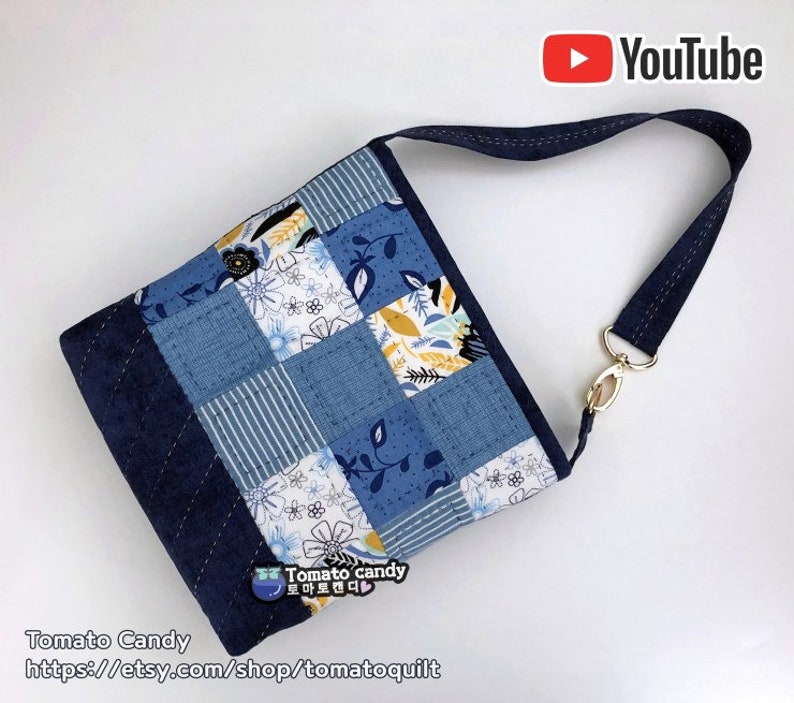 Pode incluir: Uma bolsa tote de tecido patchwork azul e branco com estampa floral. A bolsa tem uma al&ccedil;a longa ajust&aacute;vel e um fecho dourado. A bolsa &eacute; feita por Tomato Candy e o site &eacute; https://etsy.com/shop/tomatoquilt.