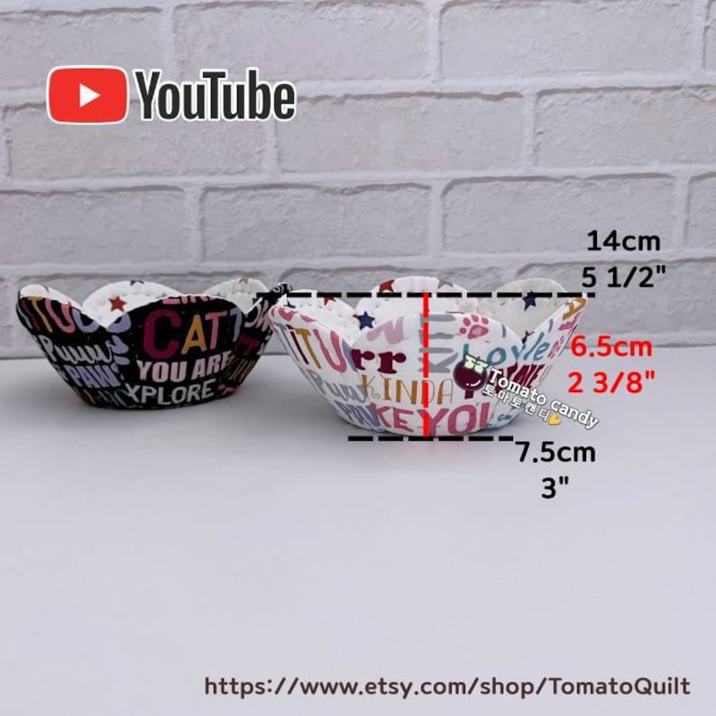 Peut inclure: Deux bols en tissu avec un bord en forme de fleur. Le bol de gauche est noir avec du texte blanc et le bol de droite est blanc avec du texte color&eacute;. Les bols mesurent 14 cm de large et 7,5 cm de haut.