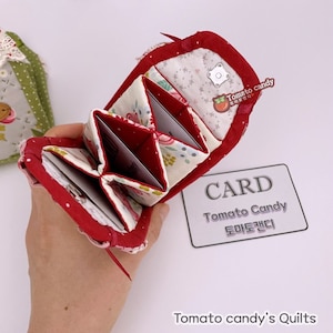 May include: A red and cream fabric accordion-style card holder with multiple interior compartments. The exterior features a red border and a snap closure. A small logo tag reads Tomato Candy, and a separate card displays the text CARD Tomato Candy.