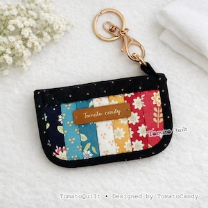 May include: A small, colorful fabric cardholder with a gold keychain. The cardholder features a patchwork design with floral and geometric patterns in various colors. The text "Tomato candy" is on a brown leather tag.