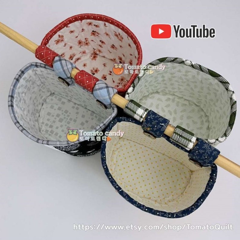 May include: Three fabric hanging baskets with different patterns. The baskets are attached to a wooden dowel rod. The baskets are lined with a white fabric with a small pattern. The baskets are made of a variety of fabrics, including plaid, floral, and geometric patterns. The baskets are labeled with the text "Tomato Candy".