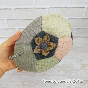May include: A small, round, quilted purse with a flower design in shades of brown, gray, and pink. The purse is made of patchwork fabric and has a gold chain.