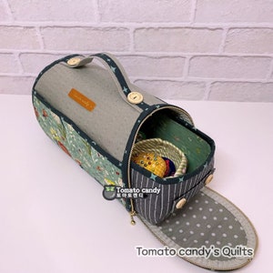 May include: A cylindrical fabric sewing organizer with a green floral print, grey textured top, and a dark green handle with star patterns. It features a zippered opening, wooden buttons, and a grey polka-dot flap. Text reads Tomato candy.