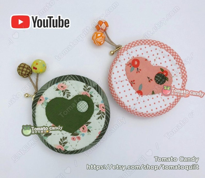 K&ouml;nnte beinhalten: Zwei runde M&uuml;nzbeutel mit herzf&ouml;rmigen Stoffakzenten. Ein Beutel ist gr&uuml;n mit einem wei&szlig;en Blumenmuster und der andere ist rosa mit wei&szlig;en Punkten. Beide Beutel haben einen kleinen Knopf und eine Stoffschlaufe mit einem kleinen orangenen Pompon.