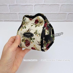 May include: A floral print pouch with a black trim, held in a hand. The pouch features a cream background with red, white, and green floral patterns. The text "TomatoCandy" is visible on the pouch.