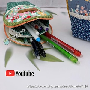 May include: A green floral patterned pencil case, open to reveal a selection of pens and markers. The case has a brown leather tag. The YouTube logo and Etsy shop URL are visible.