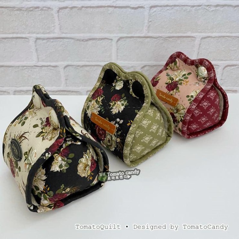 May include: Three fabric pouches with floral patterns in cream, black, and pink. Each pouch has a unique design, with a contrasting border and a button closure. The text "Tomato candy" is visible on a small label on each pouch.