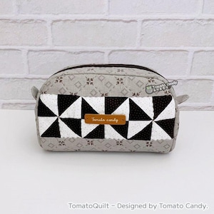 May include: A gray and white quilted makeup bag with a black and white geometric pattern. The bag has a brown leather zipper pull and a brown leather tag that says "Tomato candy".