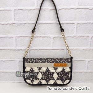 May include: A black and white quilted fabric crossbody bag with a gold chain strap. The bag has a small brown leather tag that says "Tomato candy".