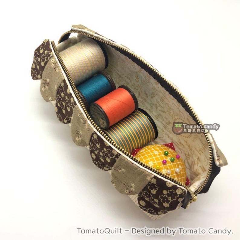 May include: A brown and beige fabric sewing case with a zipper closure. The case is filled with spools of thread in various colors, including orange, blue, and white. A small pincushion with a yellow fabric cover is also visible.