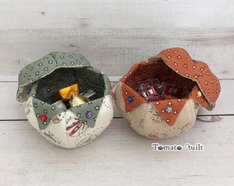 May include: Two fabric bowls with petal-shaped edges, one in sage green with star patterns and one in burnt orange with star patterns. Both feature cream-coloured bases with printed text and illustrations. Small colourful buttons adorn the petals.