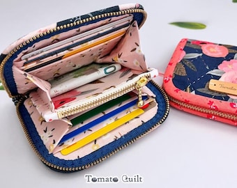 Puede incluir: Dos carteras con cremallera, exterior azul oscuro con estampado floral rosa e interior rosa claro con estampado floral. La cartera abierta muestra varias ranuras para tarjetas, un bolsillo central con cremallera y una cremallera dorada.