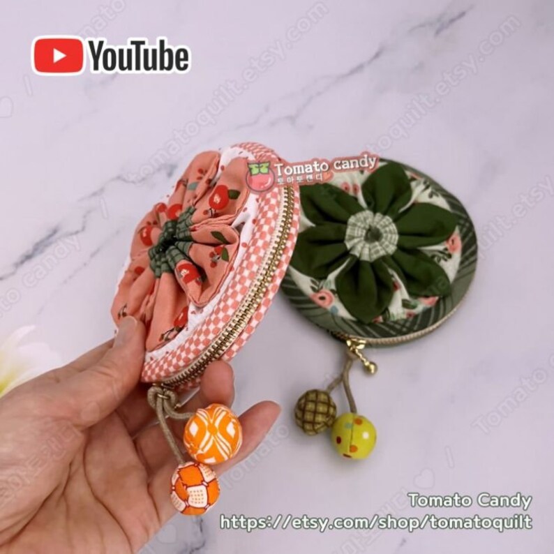 K&ouml;nnte beinhalten: Zwei runde M&uuml;nzbeutel mit floralen Stoffdesigns. Der Beutel links ist rosa mit einem Kirschendruck und der Beutel rechts ist gr&uuml;n mit einem Blumendruck. Beide Beutel haben goldene Rei&szlig;verschl&uuml;sse und Quasten.