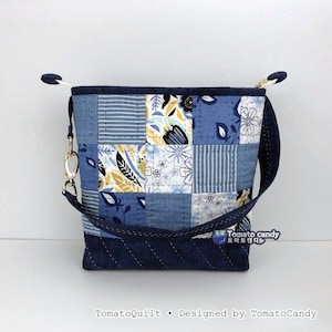 May include: A small quilted pouch featuring a patchwork design of blue, white, and yellow floral and striped patterns. The bag has a dark blue base with diagonal stitching, a gold-tone metal clasp on the side, and a dark blue strap. Text reads Tomato candy.