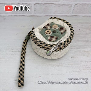 Peut inclure: Une pochette ronde en tissu blanc avec une bordure à carreaux noirs et blancs. La pochette a une fermeture éclair et une applique de hibou vert avec des boutons pour les yeux. La pochette a une sangle à carreaux noirs et blancs.