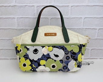 May include: A quilted handbag featuring a cream-colored upper section and a lower section with a floral pattern in shades of lime green, white, gray, and dark blue. It has dark green handles, a brown brand tag labeled Tomato candy, and a lime green button.