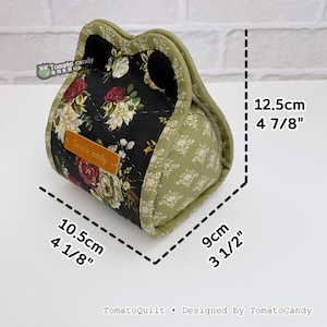 May include: A quilted fabric bag with a floral pattern on a black background, measuring 4 1/8" x 3 1/2" x 4 7/8". The bag has a green trim and a small leather tag that says "Tomato candy".