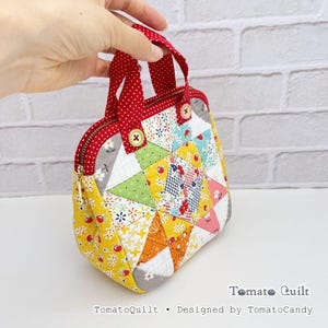 May include: A small quilted handbag featuring a patchwork star pattern in yellow, green, white, and red floral fabrics. It has red polka-dot handles, a gold-tone zipper closure, and two small wooden buttons. The text TomatoQuilt Designed by TomatoCandy is visible.