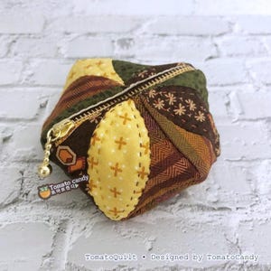 May include: A small, quilted coin purse with a gold zipper and pull. The purse features a patchwork design in shades of brown, green, and yellow. The text "Tomato candy" and "TomatoQuilt" are visible on the purse.
