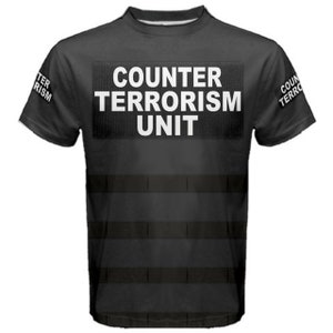 Op de afbeelding: Zwart T-shirt met een witte "COUNTER TERRORISM UNIT" patch op de voorkant. Het shirt heeft een zwart-wit gestreept patroon aan de onderkant.
