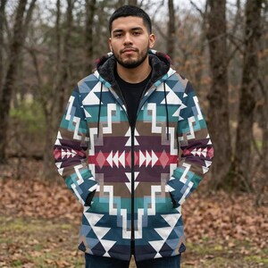 May include: A patterned hooded jacket in blue, teal, brown, and red. The jacket features a black fur-lined hood and a full zip. The person is wearing a black top. The background is a blurred forest. The jacket's design is geometric.
