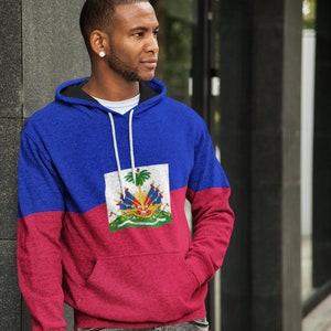 May include: A blue and red hoodie with the flag of Haiti printed on the front. The flag features a coat of arms with a palm tree, a cannon, and a drum.
