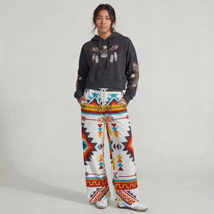 May include: A charcoal gray hoodie with an embroidered eagle design and matching patterned pants. The pants feature a white background with colorful geometric and arrow patterns. The outfit is casual and comfortable.