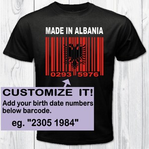 Può includere: Maglietta nera con il testo "MADE IN ALBANIA" e un codice a barre con la bandiera albanese. Il codice a barre ha i numeri "0293 5976" sotto. Il testo "CUSTOMIZE IT! Add your birth date numbers below barcode. eg. "2305 1984"" è sotto il codice a barre.