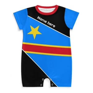 Op de afbeelding: Een blauwe, zwarte en rode babyromper met een gele ster en de tekst "Name here". De romper heeft korte mouwen en een ronde hals met een rode bies. Het ontwerp lijkt op een vlag.
