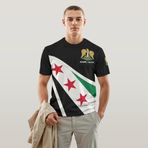May include: A black t-shirt with a diagonal design featuring the Syrian flag. The flag has three red stars, a green and white stripe, and the Syrian coat of arms. The text "NAME HERE" is printed on the shirt.