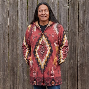 May include: A red hooded coat with a geometric pattern in black, yellow, and white. The coat has a toggle closure and a soft, textured lining. The coat is worn over a black shirt.