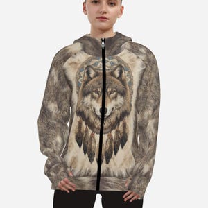 May include: A zip-up hoodie featuring a detailed wolf illustration with feathers and a circular design. The hoodie has a fur-like pattern on the sleeves and hood, with a black zipper. The wolf design is centered on a beige background.