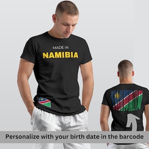Puede incluir: Camiseta negra con la inscripción "MADE IN NAMIBIA" en amarillo. La camiseta presenta la bandera de Namibia en la parte delantera y un diseño de código de barras con la bandera y una fecha en la parte trasera. La camiseta es de cuello redondo.