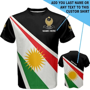 May include: Black t-shirt with a diagonal design featuring the flag of Kurdistan. The flag has a red, white, and green stripe with a yellow sun in the center. The shirt has the text "NAME HERE" on the front.