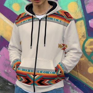 May include: Cream zip-up hoodie with a black hood lining and zip. The hoodie showcases a Southwestern-style geometric pattern in red, orange, turquoise, and grey across the shoulders and cuffs. It has a front pocket and a silver chain necklace.