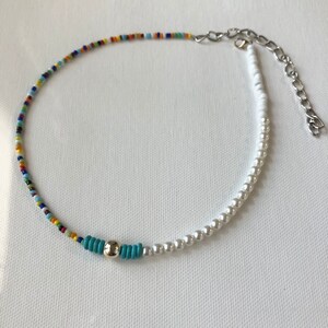 May include: A colorful beaded necklace with a silver charm and white pearl beads. The necklace is made of small, colorful beads and white pearls.