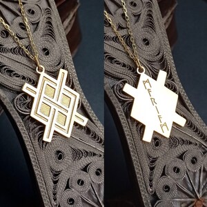 May include: A gold necklace with a pendant featuring a geometric design. The pendant is engraved with the word "MERKIVA".