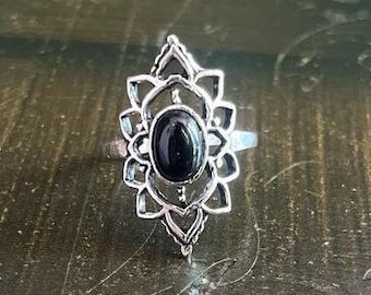 Puede incluir: Un anillo de plata con una piedra preciosa negra engastada en un diseño floral decorativo.