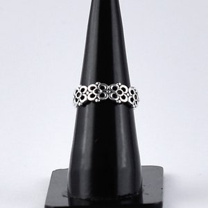 Peut inclure: Une bague en argent avec un motif floral. La bague est sur un présentoir noir.