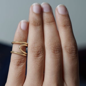 Puede incluir: Un anillo de oro con un diseño de doble banda. El anillo se lleva en el dedo índice de una mano.