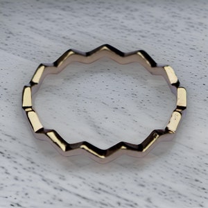 Puede incluir: Un anillo de color dorado con un patrón en zigzag. El anillo está hecho de metal y tiene un acabado liso.