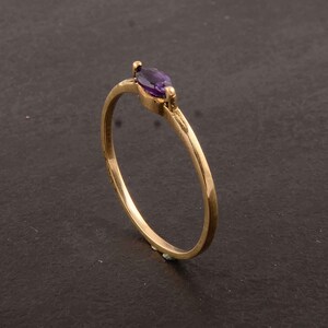 以下が含まれることがあります： マルキーズ型のアメジストの宝石が1つ付いた、繊細な金の指輪です。
