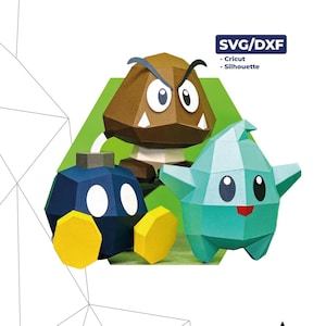 Puede incluir: Modelos de papel de Goomba, Bob-omb y Luma, con el texto "Bomba, Goomba y Luma". Los modelos son de papel y tienen formas geométricas. Las dimensiones son 14 cm x 13 cm x 13 cm.