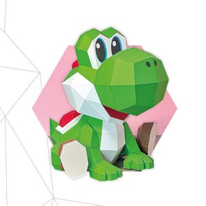 Puede incluir: Un modelo de papel de Yoshi verde y blanco con detalles en rojo, sobre un fondo rosa. El modelo está hecho de 54 piezas y mide 23 cm x 23 cm x 25 cm. El texto "YOSHI" está en la parte superior.