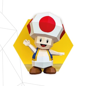 Puede incluir: Figura de papel de Toad, personaje de Mario. La figura es blanca con un gorro de hongo rojo con lunares, chaleco azul y zapatos marrones. Dimensiones: 23 cm x 16 cm x 14 cm. El texto "TOAD" es visible.