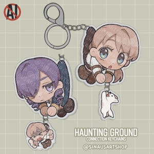 Puede incluir: Dos llaveros acrílicos con ilustraciones de personajes de estilo anime. Un llavero muestra un personaje con cabello morado y otro con cabello castaño claro, ambos con un diseño chibi. Los llaveros están conectados a una cadena y un cierre plateados. El texto "HAUNTING GROUND CONNECTION KEYCHAINS @SINAUSARTSHOP" es visible.