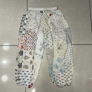 以下が含まれることがあります： 様々な花柄と幾何学模様が施された白いパッチワークパンツ。パンツはゴムウエストとドローストリング付きです。