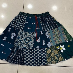 May include: A dark green patchwork skirt with a white drawstring. The skirt is made of different fabrics with various patterns, including paisley, polka dots, and floral designs.