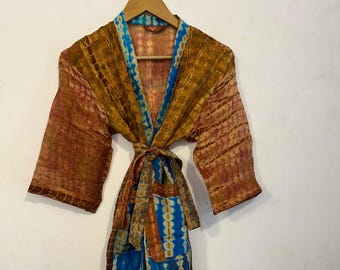 May include: A tie-dye patterned robe in shades of brown, orange, and blue hangs on a wooden hanger. The robe features a V-neck design and a matching tie belt. The fabric has a textured appearance.