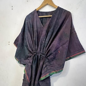 May include: A dark purple kaftan dress with a V-neck and wide sleeves, hanging on a wooden hanger. The dress has a drawstring waist and is trimmed with green and red stitching along the edges.